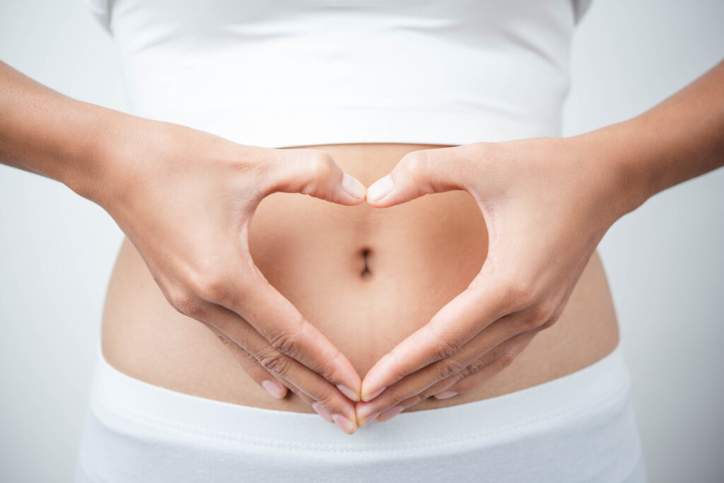 Close-up of a woman's hands forming a heart shape on her belly