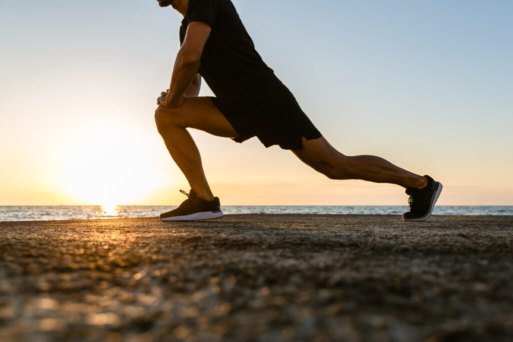 A man performing dynamic stretching on the beach during sunset, symbolizing the benefits of movement and physical therapy