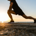 A man performing dynamic stretching on the beach during sunset, symbolizing the benefits of movement and physical therapy