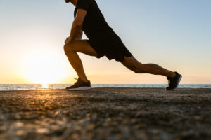 A man performing dynamic stretching on the beach during sunset, symbolizing the benefits of movement and physical therapy