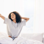 Person waking up and stretching in bed, feeling well-rested and refreshed after a good night’s sleep.